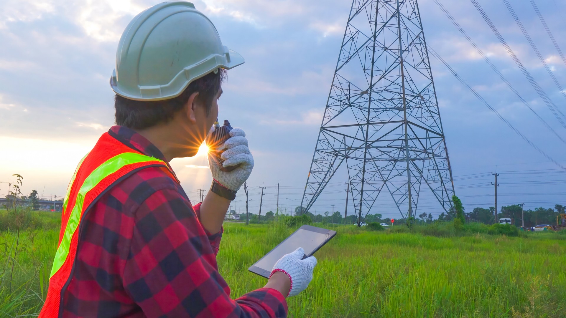 Engineering in standard safety uniform working inspect the electricity high voltage pole with tablet near tower with electricity.
